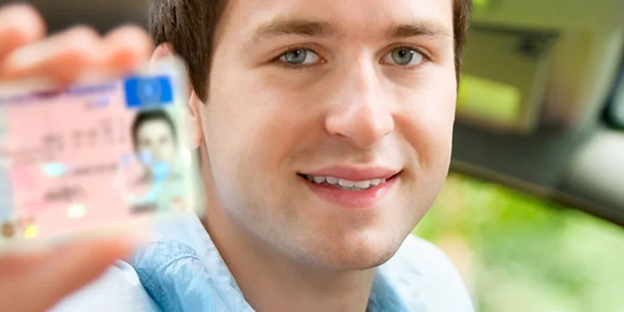 Young driver holding his new driver's license in the car